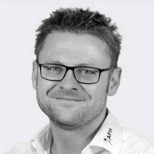Smiling man with short hair and black-framed glasses in a white collared shirt.